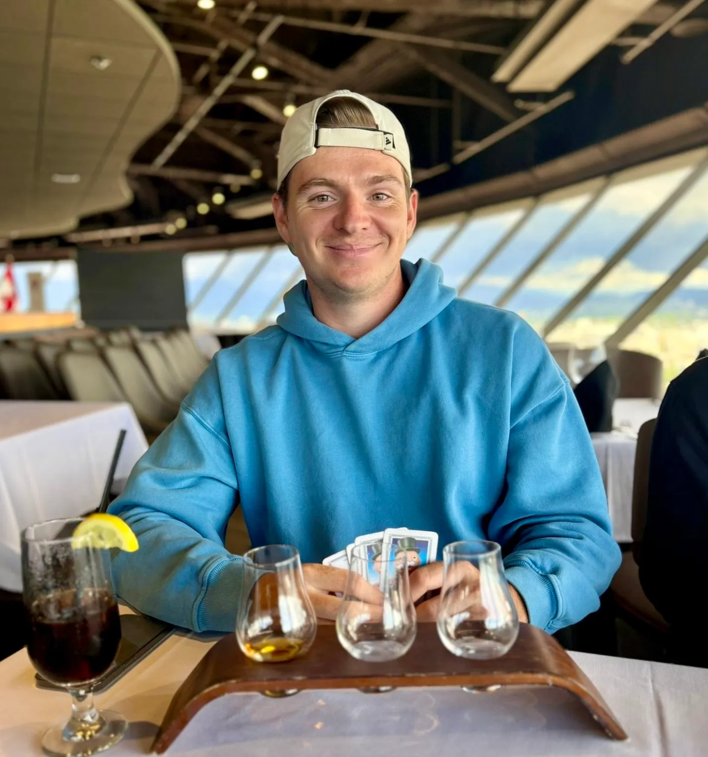 Niklas im blauen Hoodie an einem Tisch mit Whisky-Probiergläsern, im Hintergrund die Fensterfront des Vancouver Lookout